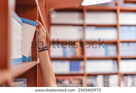 Close up of a woman hand taking out a book from the bookshelf at the library