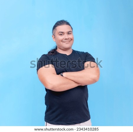 A happy and proud looking biracial male smiling confidently with arms crossed. Isolated on a blue background.