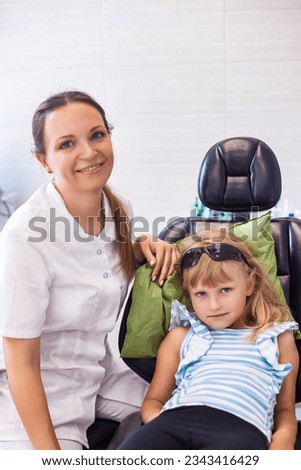 Portrait of little girl 5-6 year old visit dentist doctor, sitting in medic chair, looking at camera. Kid girl treating teeth at dental office. Medical children dentistry concept. Copy ad text space