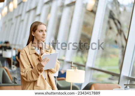 Thoughtful girl student using digital tablet looking away. Young woman holding tab computer modern tech device standing in university campus, coworking office space and thinking. Copy space
