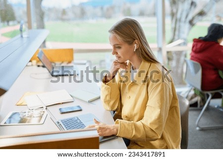 Teen girl student using laptop looking at computer sitting at desk in university college campus classroom hybrid learning online,watching webinar class, elearning or remote working in coworking. Royalty-Free Stock Photo #2343417891