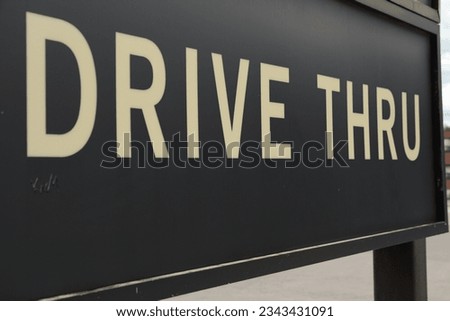 drive thru sign in white capital letters on black background with black leg, parking lot somewhat visible in background