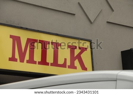 sign that says milk in red capital letters on yellow horizontal sign background against building wall with delivery vehicle hood in foreground