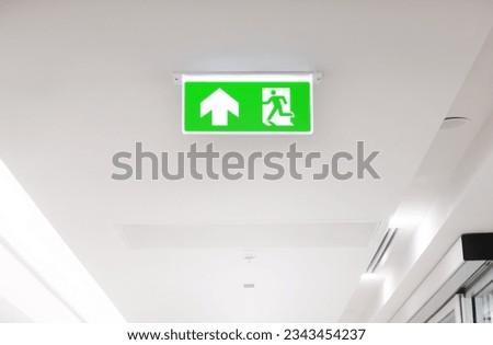 Lighted glowing green emergency exit signs in an office hallway with arrows pointing the way out of the building.