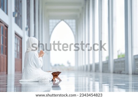 The image of an Asian Muslim woman in the Islamic religion in hijab in cream color. reading the Quran and having a happy Staying in a beautiful mosque, Arabic word translation: The Holy Al Quran. Royalty-Free Stock Photo #2343454823