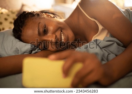 Young woman using a smart phone while waking up in the morning in the bedroom