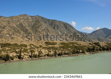 A fragment of a wide turquoise river with high rocky banks with rare high dreams flowing through a beautiful valley at the foot of a mountain range. Katun river, Altai, Siberia, Russia. Royalty-Free Stock Photo #2343469861