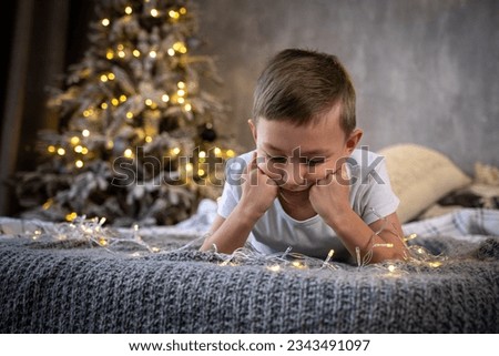 a sad boy before the Christmas holiday lies on the bed next to the Christmas tree