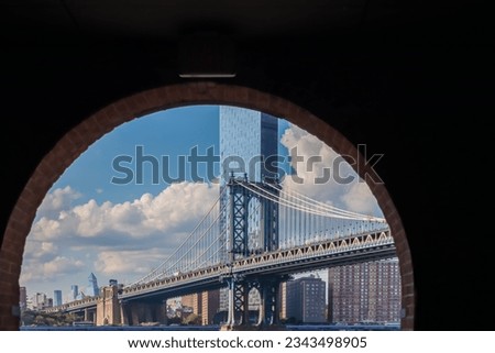 Iconic Manhattan Bridge connecting New York City's urban landscape with stunning skyline and architectural marvel, seen through a bricked wall. Tall skyscrapers. Famous spot for sightseeing