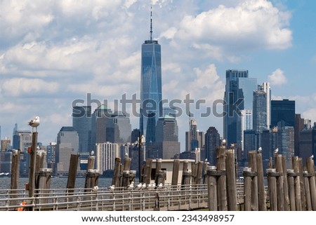 A wooden pier on the Hudson River with captivating New York urban skyline with striking and modern skyscrapers in the back, seen from The Battery Park. Think clouds above the city. Modern city. Royalty-Free Stock Photo #2343498957