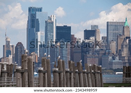 A wooden pier on the Hudson River with captivating New York urban skyline with striking and modern skyscrapers in the back, seen from The Battery Park. Think clouds above the city. Modern city. Royalty-Free Stock Photo #2343498959