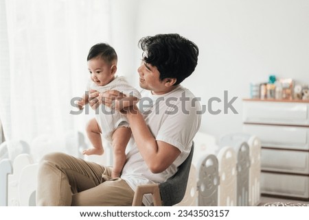 Happiness of fatherhood. Young Asian dad with adorable baby on his hands sitting near window at home. Loving father spending time with infant child. Fathers day concept. Royalty-Free Stock Photo #2343503157