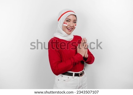 A friendly Indonesian muslim woman is wearing red top and white hijab gesturing traditional greeting to celebrate Indonesia Independence Day. Isolated by white background.