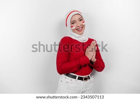 A friendly Indonesian muslim woman is wearing red top and white hijab gesturing traditional greeting to celebrate Indonesia Independence Day. Isolated by white background.