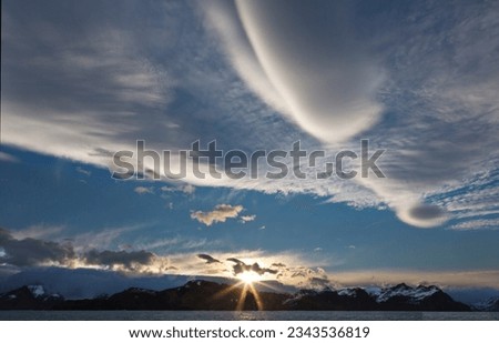 Lenticular cloud before sunrise; Prince Olav Harbour, South Georgia; Lenticular clouds and sun-star over the mountains of South Georgia