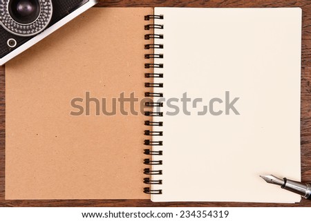 Blank notebook and pen with camera on wooden background.