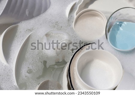 Dishes and bowls in water and bubbles of dishwashing liquid. Kitchen work