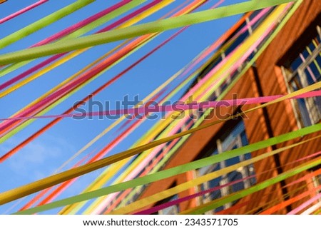 Multicoloured ribbons stream between buildings against a blue sky. Royalty-Free Stock Photo #2343571705