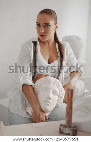 Talented female sculptor in a white shirt and jeans, holding an ancient Greek bust in her workshop, surrounded by tools. A perfect blend of craftsmanship and artistry