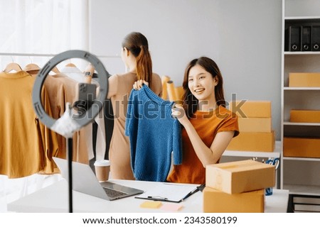 Fashion blogger concept, Young Asian women selling clothes on video streaming.Startup small business SME, using smartphone or tablet taking receive and checking in office
