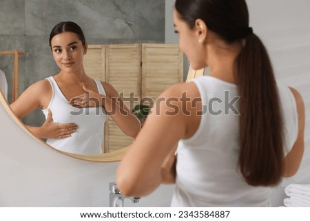 Beautiful young woman doing breast self-examination near mirror in bathroom Royalty-Free Stock Photo #2343584887