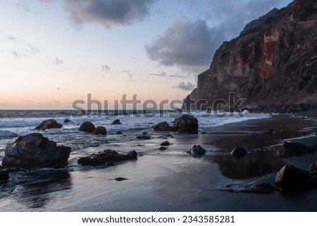 Scenic view during sunset on volcanic black sand beach Playa del Ingles in Valle Gran Rey, La Gomera, Canary Islands, Spain, Europe. Massive cliffs of the La Mercia range. Smooth waves sweeping rocks Royalty-Free Stock Photo #2343585281