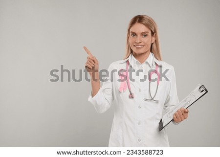 Doctor with pink ribbon, clipboard and stethoscope on light grey background, space for text. Breast cancer awareness