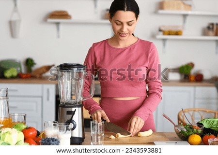 Sporty young woman cutting banana in kitchen Royalty-Free Stock Photo #2343593881