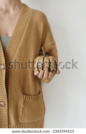 Young woman in beige knitted cardigan hold in hand decorative pumpkin over white wall Royalty-Free Stock Photo #2343594515