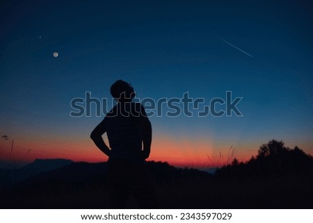 Man looking at the starry skies, crescent Moon and shooting star in blue hour twilight time. Royalty-Free Stock Photo #2343597029