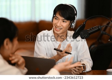 Handsome male radio host wearing headphone interviewing guest, recording podcast at home studio