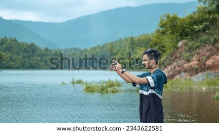 Happy confident male in casual clothes standing near mountain and taking photos on mobile phone during trekking trip 