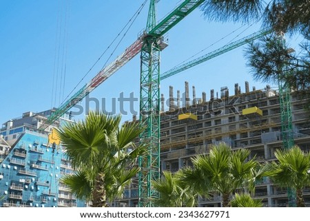 Close-up of a construction crane against the background of buildings, palm trees, blue sky. Beautiful construction site