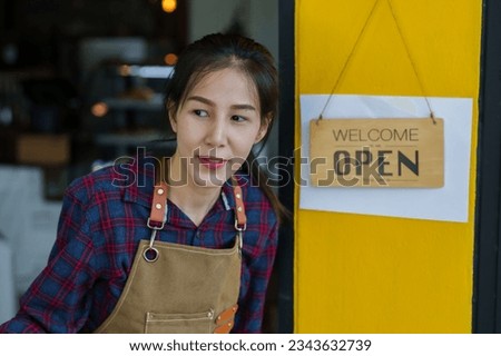 Beautiful Asian woman wearing apron Open the door to look outside of the coffee shop. to see if customers will come, and the front of the store has a sign that says open