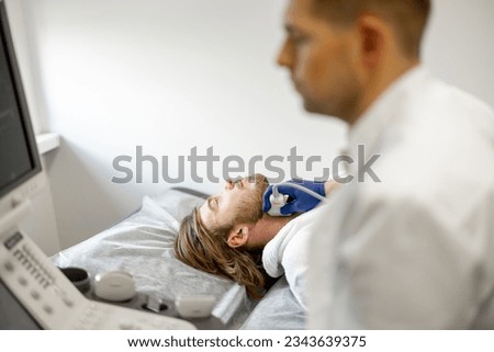 Young guy during an ultrasound diagnosis of the carotid artery. Concept of ultrasound diagnostics and men's health. Idea of examination of cardiovascular diseases Royalty-Free Stock Photo #2343639375