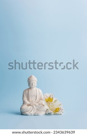 Happy Buddha Day with Siddhartha Gautama statue with flowers on blue background. Vesak Day. Mental health and meditation concept. Selective soft focus, copy space