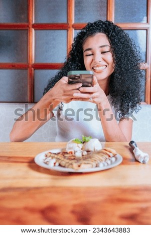 Happy girl photographing a plate of chocolate crepe and ice cream. Young woman using cell phone and taking a picture of chocolate crepe