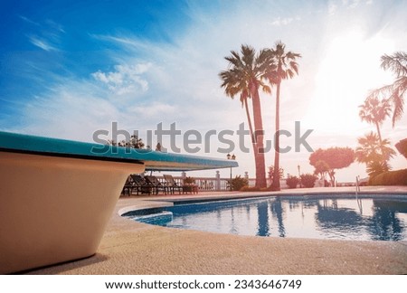 Close-up of a diving board over the open swimming pool during sunset light through south palm trees on hot summer evening Royalty-Free Stock Photo #2343646749