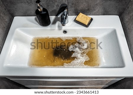 Clogged white sink in bathroom, sink with dirty water, brown soap. Plumbing problems. Royalty-Free Stock Photo #2343661413