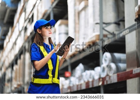 Worker in blue dress inspects, handles goods in a warehouse. Female worker using tablet working in logistic export-import industry.