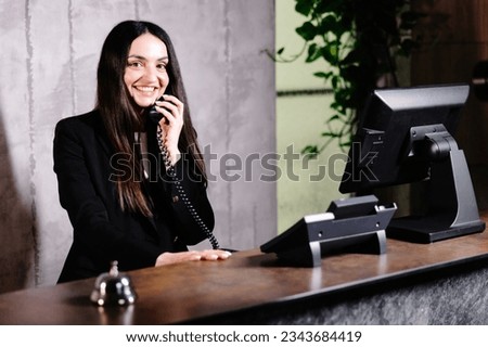 Hotel receptionist. Modern hotel reception desk with bell. Happy female receptionist worker standing at hotel counter and talking to phone Royalty-Free Stock Photo #2343684419