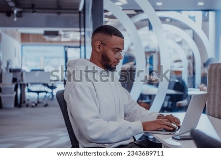 In a modern office setting, an African American businessman is diligently working on his laptop, embodying determination, ambition, and productivity in his professional environmen Royalty-Free Stock Photo #2343689711