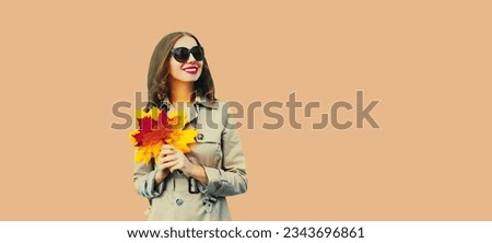 Portrait of beautiful young woman with yellow maple leaves looking up wearing jacket, sunglasses on brown wall studio background, blank copy space for advertising text
