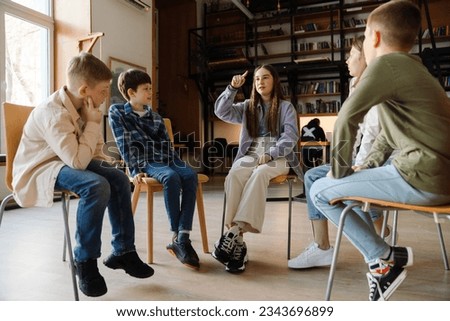 Group of schoolkids discussing something while sitting in circle on chairs in library Royalty-Free Stock Photo #2343696899
