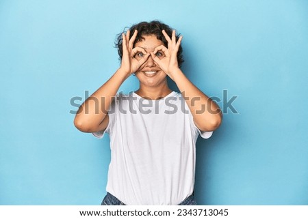 Young Caucasian woman with short hair showing okay sign over eyes
