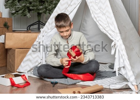 Gift wrapping. A teen child wraps Christmas gifts surprises in kraft paper with a rope, red ribbons. A serious boy is packing gifts for the family. Family Christmas