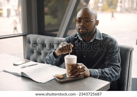 Black man sitting in a cafe with a cup of latte and papers