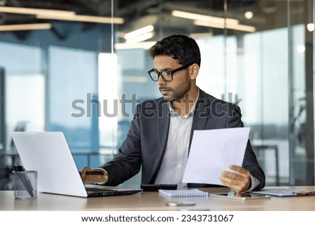 Serious concentrated hispanic businessman financier on paperwork inside office, man in business suit at workplace reviewing and reading papers, contracts and accounts reports Royalty-Free Stock Photo #2343731067