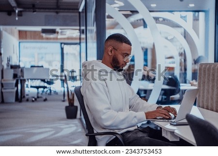 In a modern office setting, an African American businessman is diligently working on his laptop, embodying determination, ambition, and productivity in his professional environmen Royalty-Free Stock Photo #2343753453