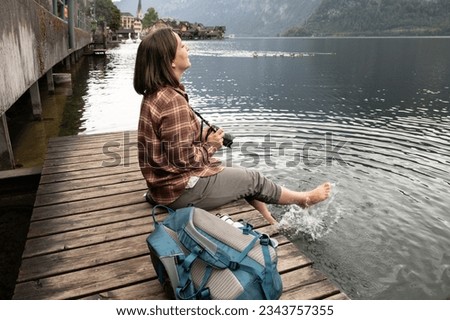 Young female photographer sitting on a wooden bridge by the water and splashing her feet, Hallstatt, Austria Royalty-Free Stock Photo #2343757355